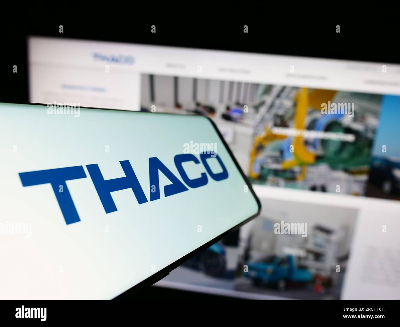 Smartphone with logo of company Truong Hai Auto Corporation (THACO) on screen in front of website. Focus on center-left of phone display. Stock Photo