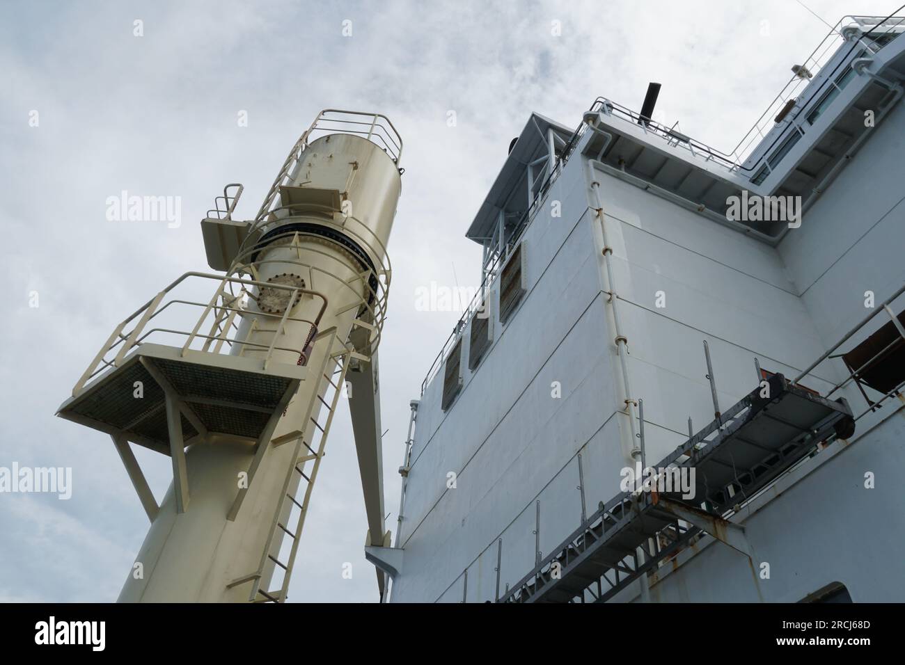 Aft part of white superstructure and cream cargo crane of container vessel observed from main deck. Stock Photo