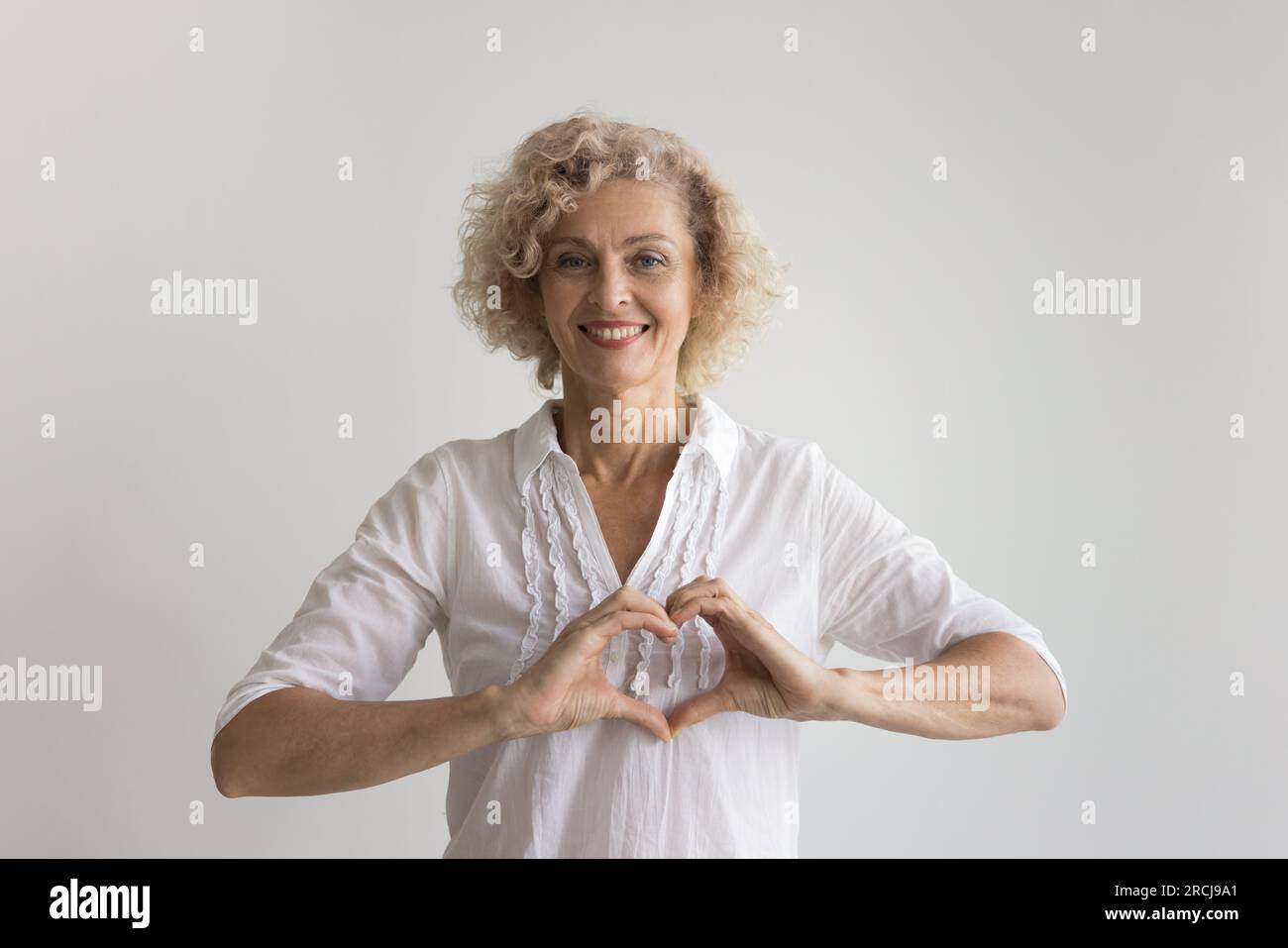 Happy pretty mature lady making heart shaped fingers Stock Photo
