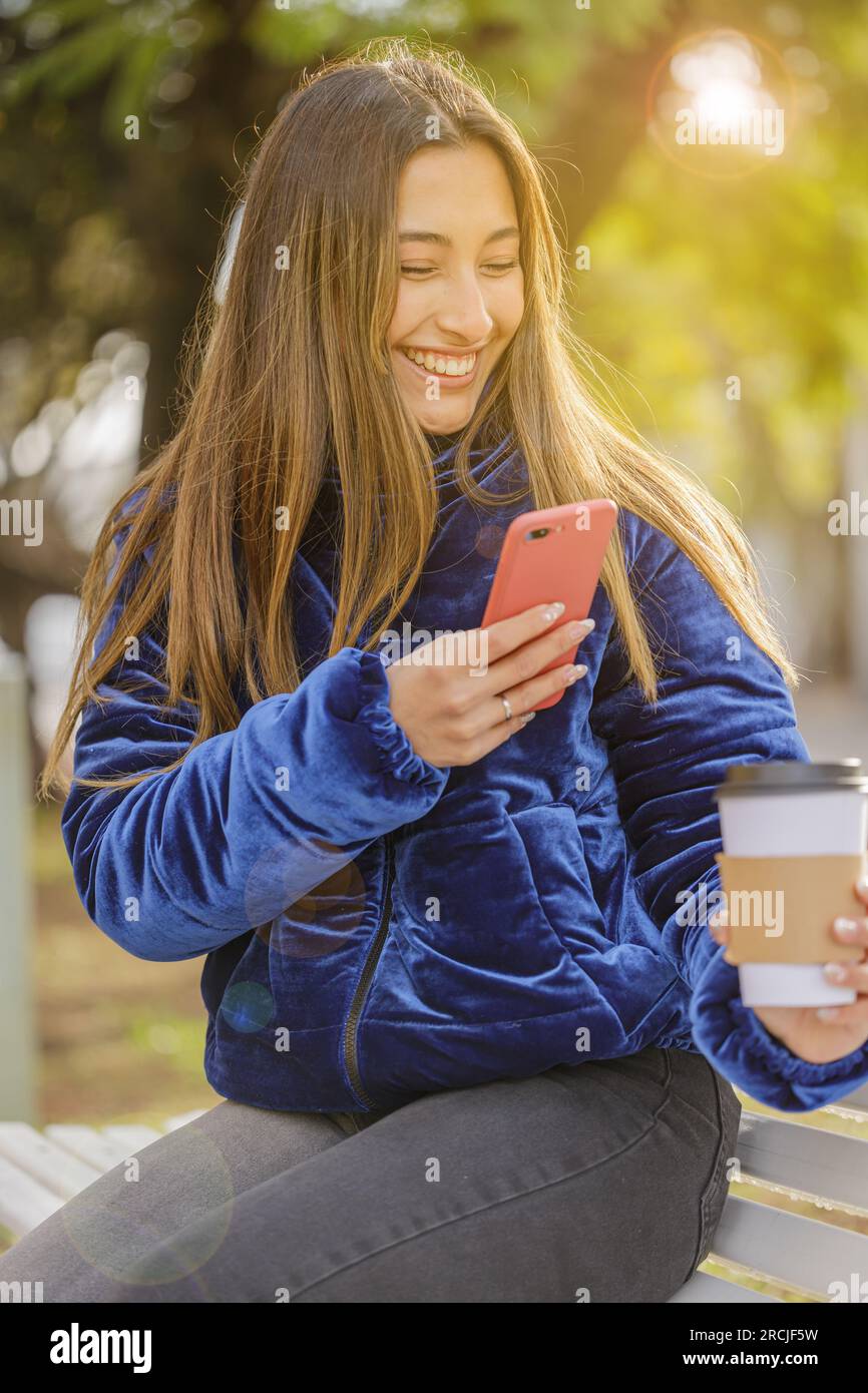 Latina girl taking a picture with her mobile phone of a disposable cup of coffee in a public park. Stock Photo