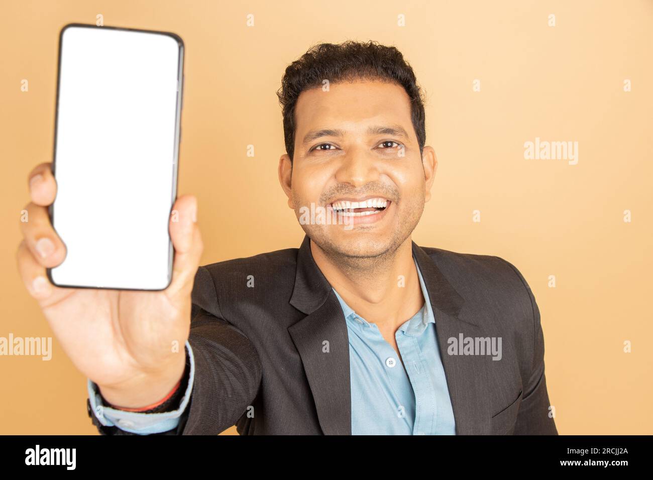 Young indian businessman wearing suit showing smart phone with blank display screen to put advertisement isolated over white background. Corporate Con Stock Photo