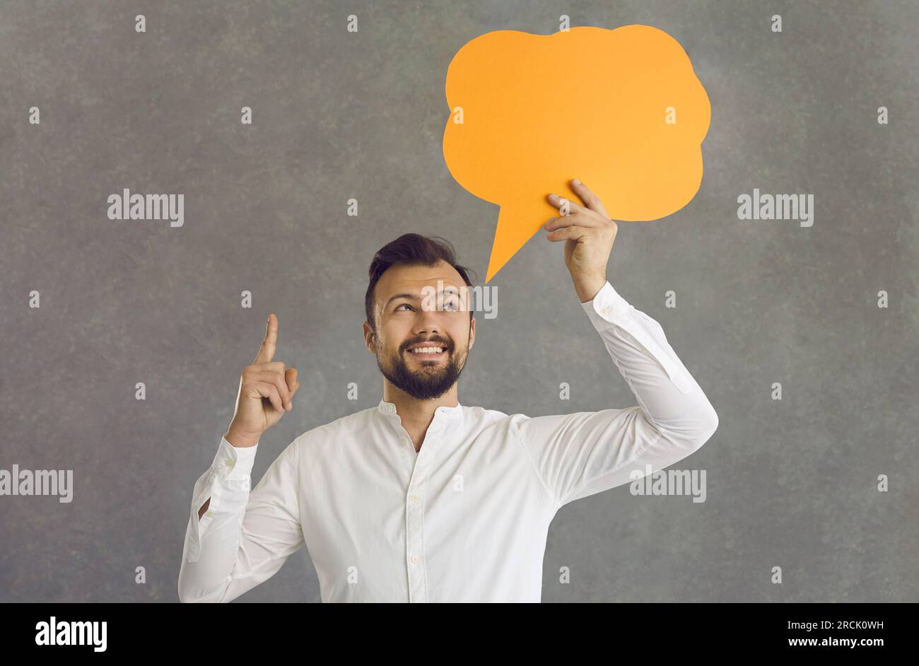 Excited man having idea holding speech bubble standing over grey background Stock Photo