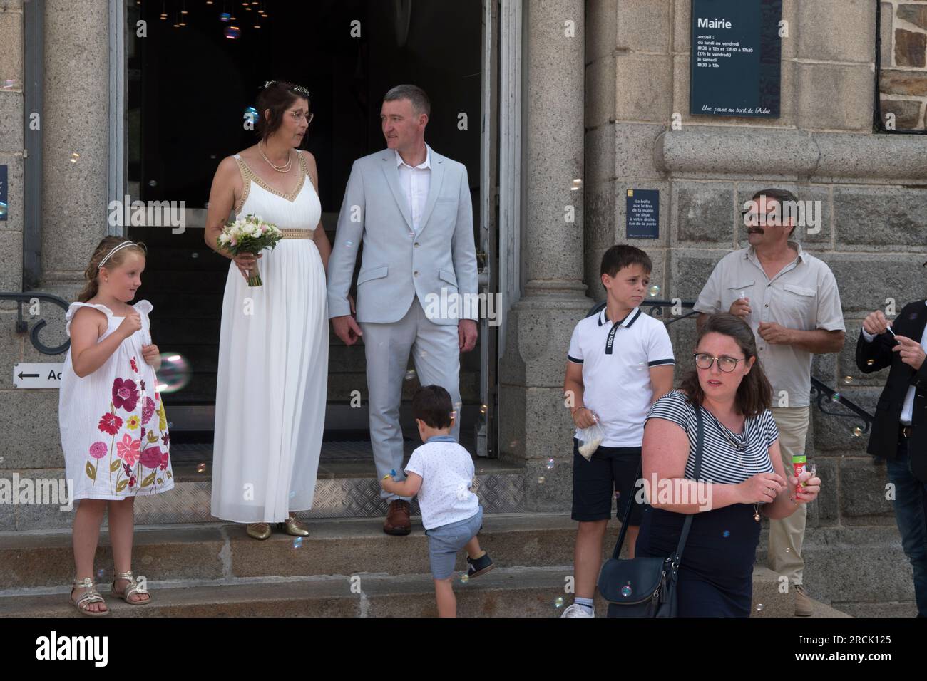 Wedding party the middle aged couple with their children on the steps of the town hall. Guests blow bubbles instead of throwing confetti. Chateaulin, Brittany, France 8th July 2023. 2020s HOMER SYKES Stock Photo