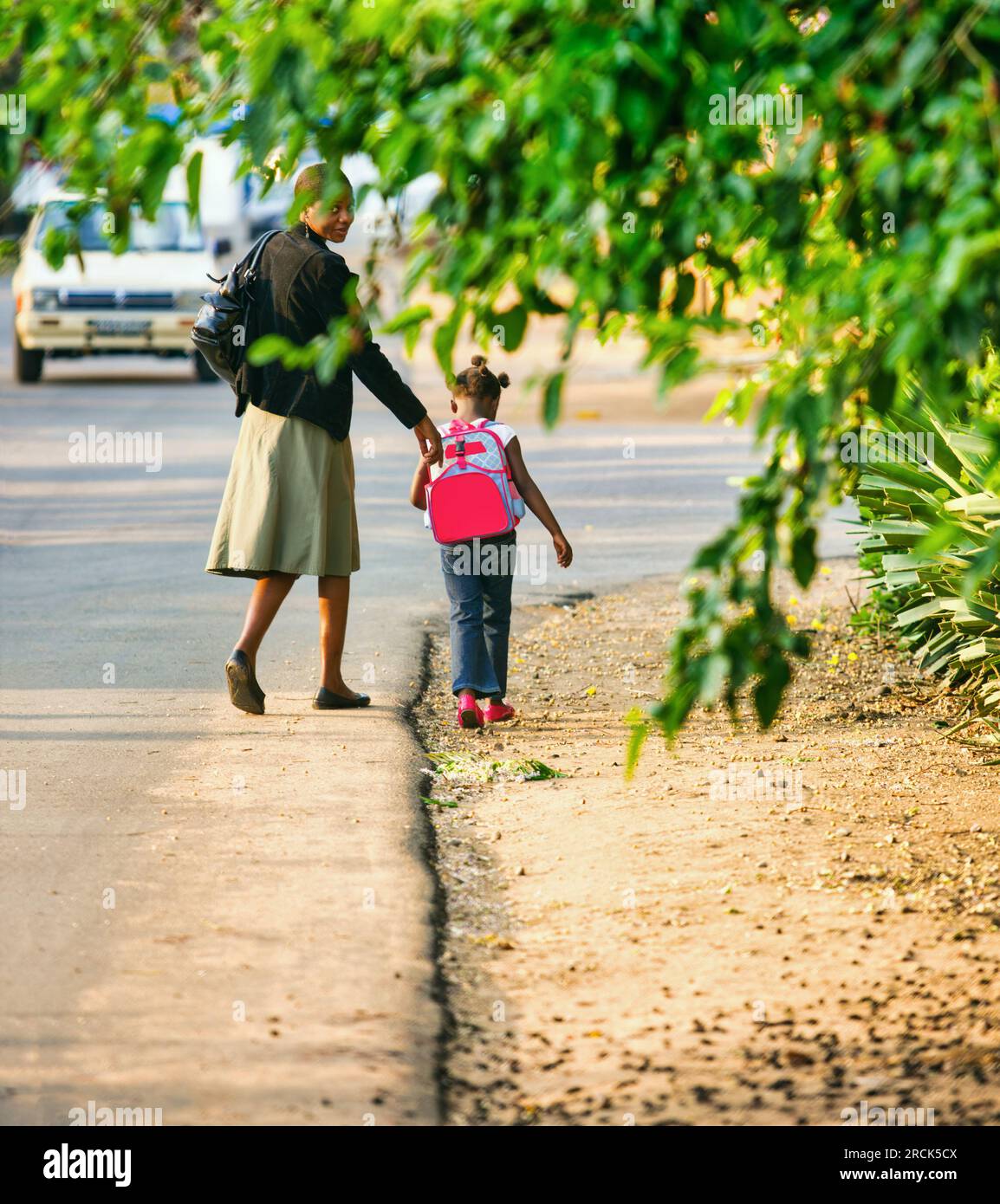 back to school, mother and small african girl with a backpack walking