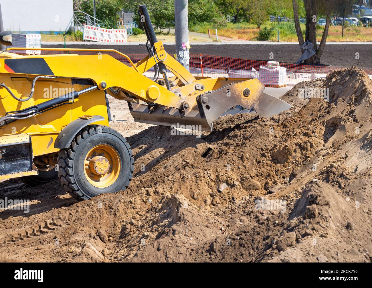 The metal sliding bucket of the wheeled bulldozer rakes a pile of sand at the workplace. Stock Photo