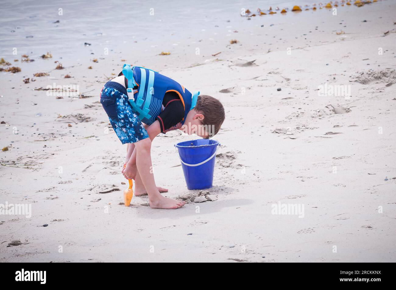 A little boy is digging the beach sand from between his legs, He said,' that is where the best sand is.' Out of eight miles only that sand was best. Stock Photo