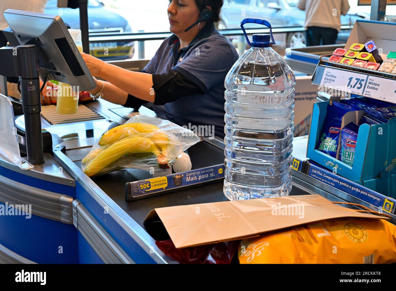 Cashier at supermarket with prices items with food and bottle water on conveyor belt Stock Photo
