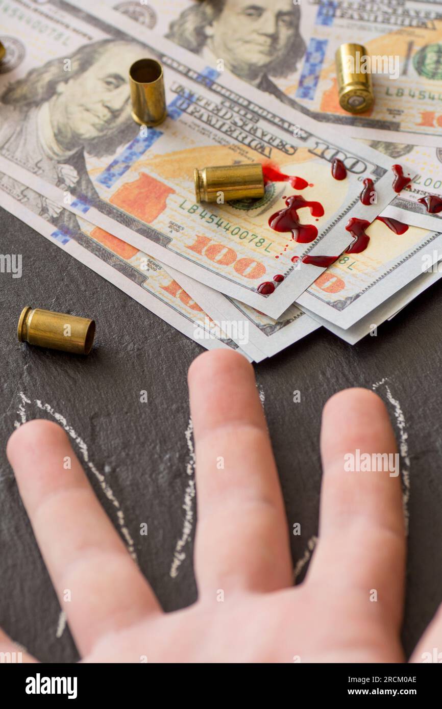 spat blood on hundred dollar bills and fire arm cartridges and body part outline crime scene dirty money concept Stock Photo