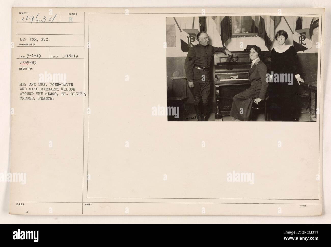 Mr. and Mrs. Ross-David and Miss Margaret Wilson gathered around a piano in St. Dizier, Creuse, France. The photo was taken on January 16, 1919, by Lt. Fox and received on March 1, 1919. The image is numbered 49634 and its description is 2583-19. Stock Photo