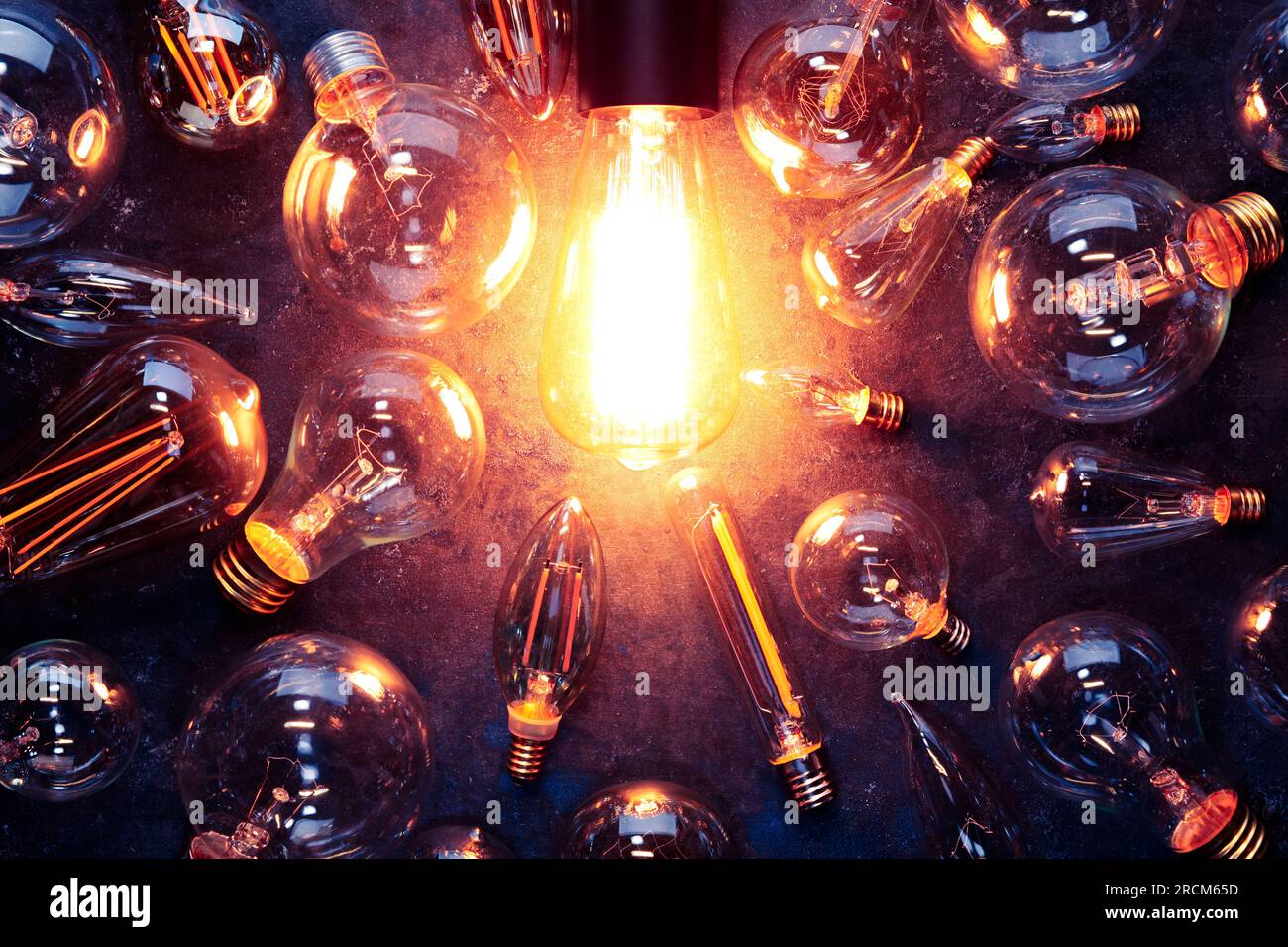 Vintage old light bulb glowing yellow on rough dark background surrounded by burnt out bulbs. Idea, creativity concept. Stock Photo