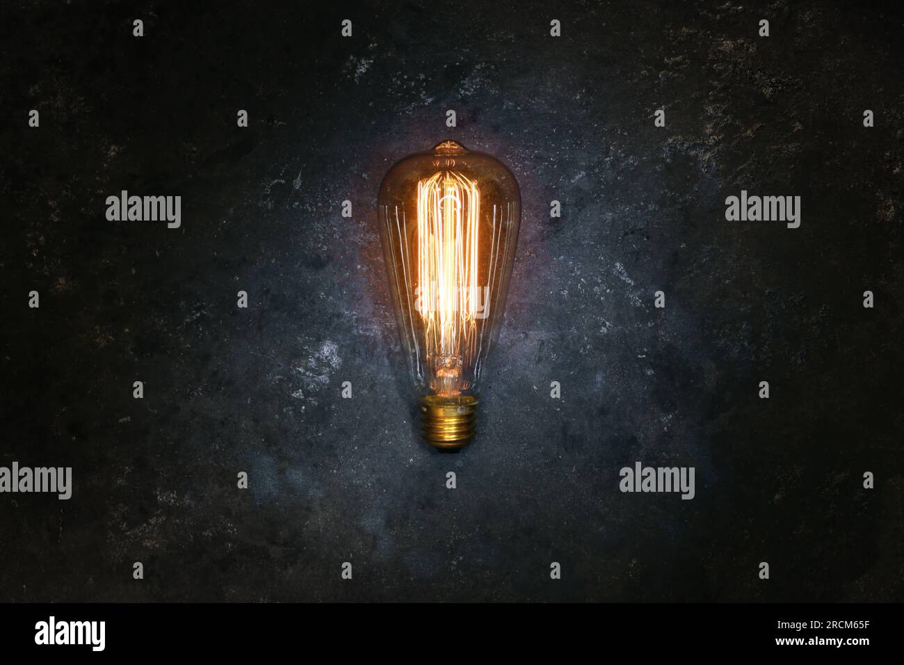 Vintage old light bulb glowing yellow on rough dark background. Idea, creativity concept. Stock Photo