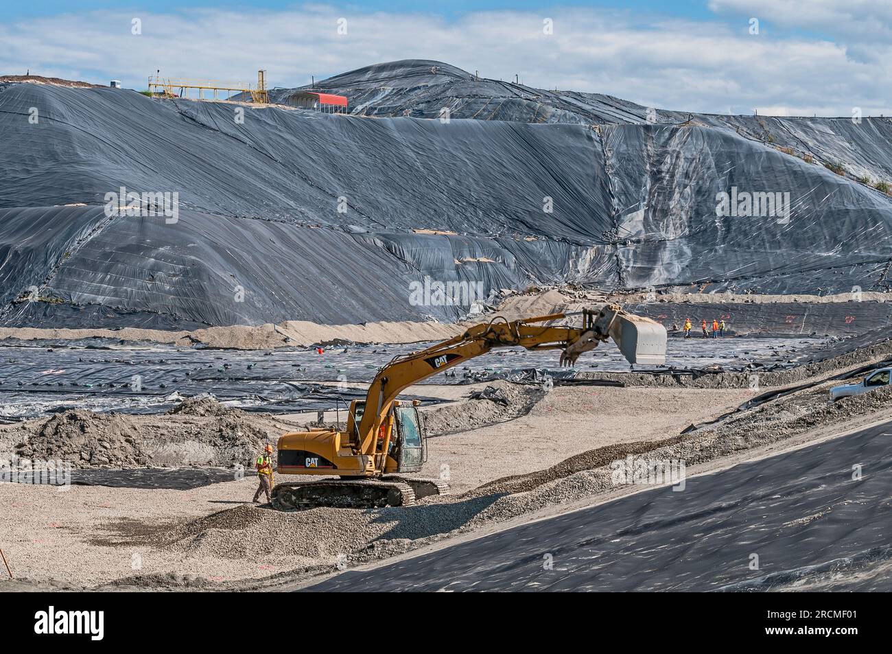 Workers and a power shovel work to excavate and install geomembrane in