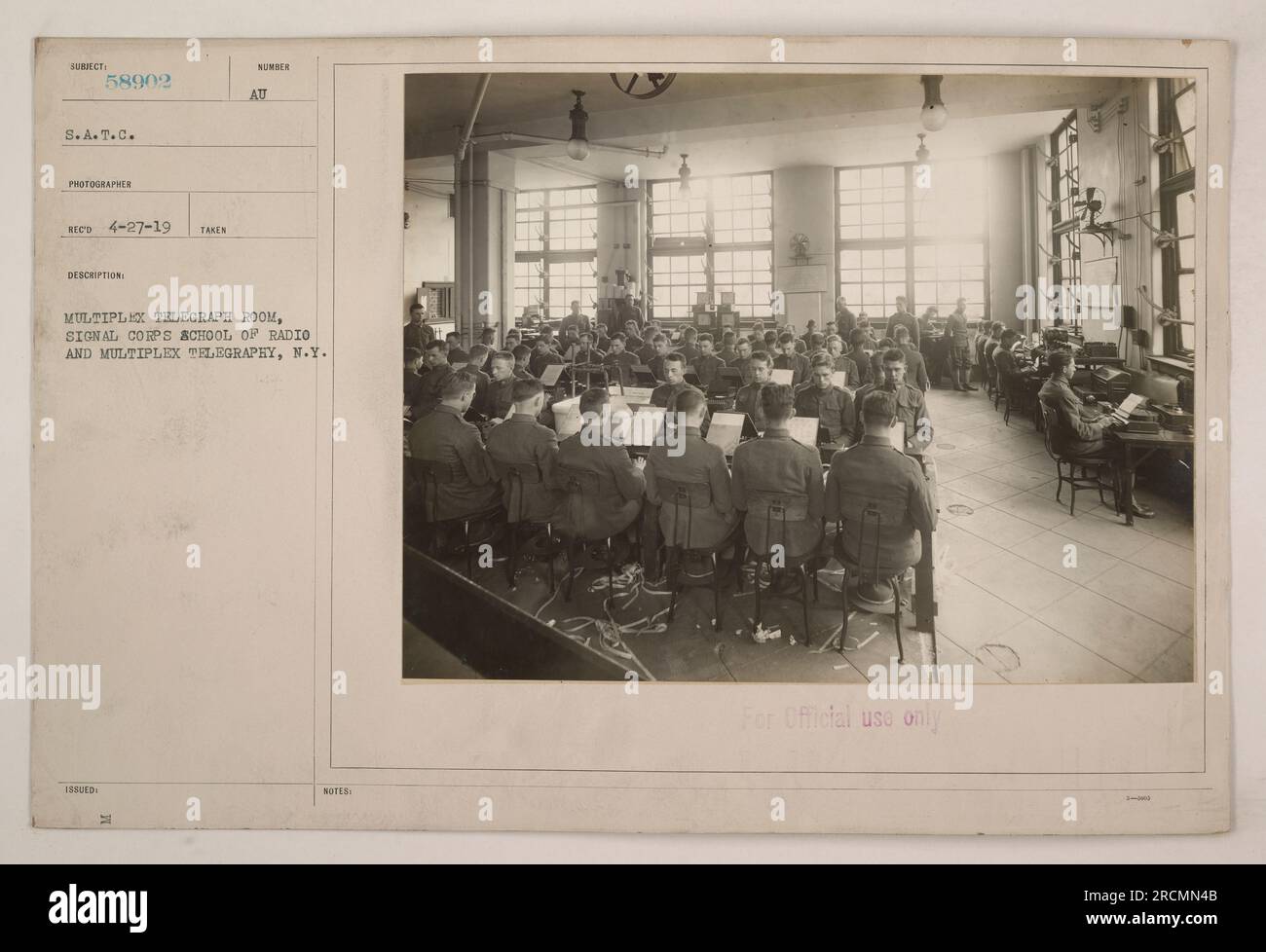 A photograph taken on April 27, 1919, in the Multiplex Telegraph Room of the Signal Corps School of Radio and Multiplex Telegraphy in New York. The image shows equipment and operators working in the room. It is labeled with the subject number 58902 and is marked for official use only. Photographer: Reed. Stock Photo