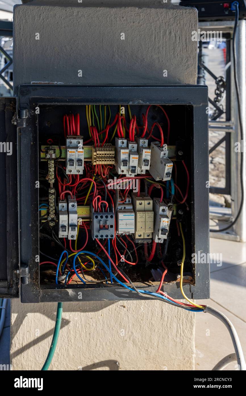 unsafe electric panel with power arrestors and breakers, wrongly wired, and cables exposed on the wall of a building Stock Photo