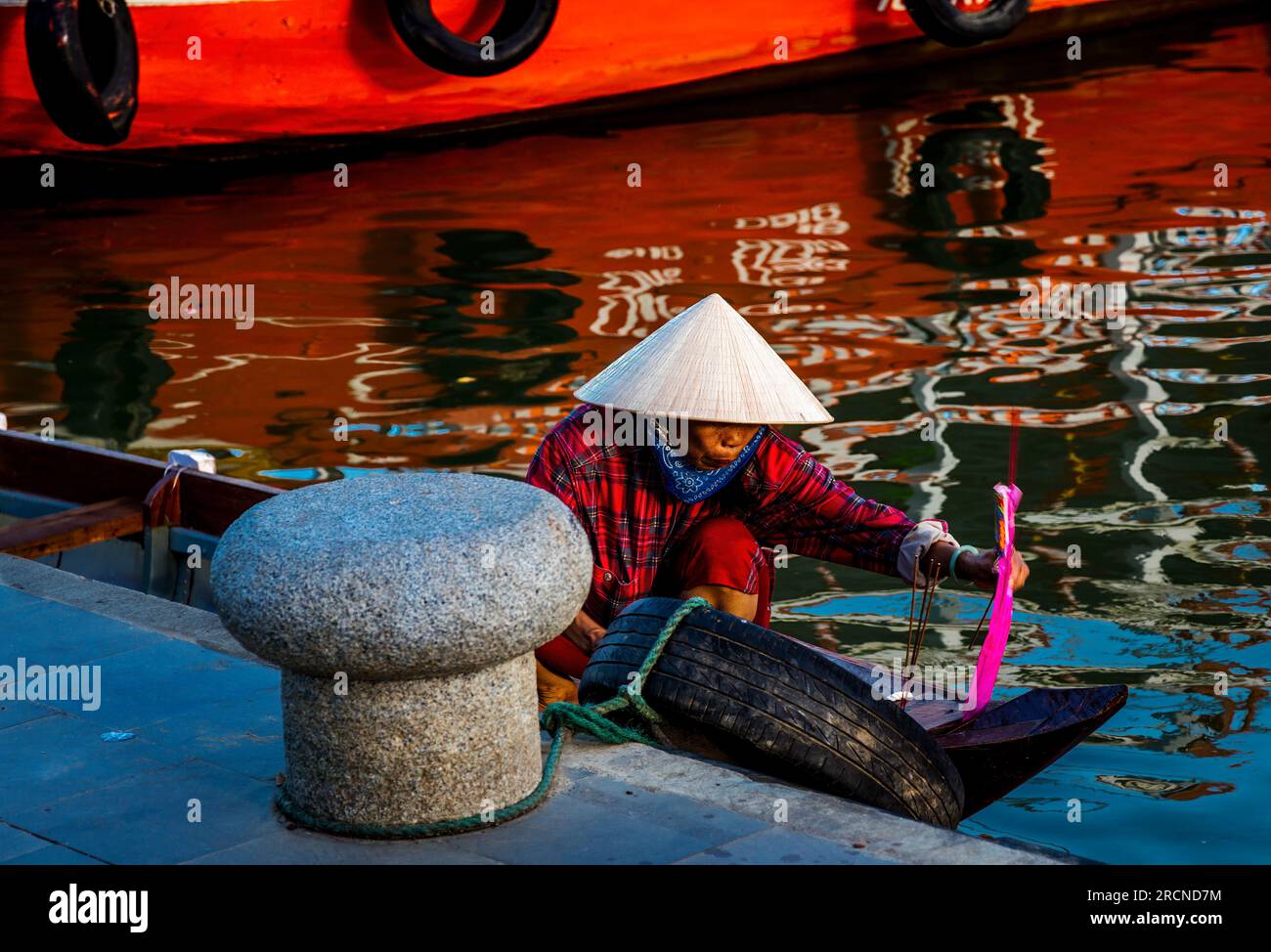 A Vietnamese woman next to a dock maneuvers her small tour boat in the Old City of Hoi An. Stock Photo
