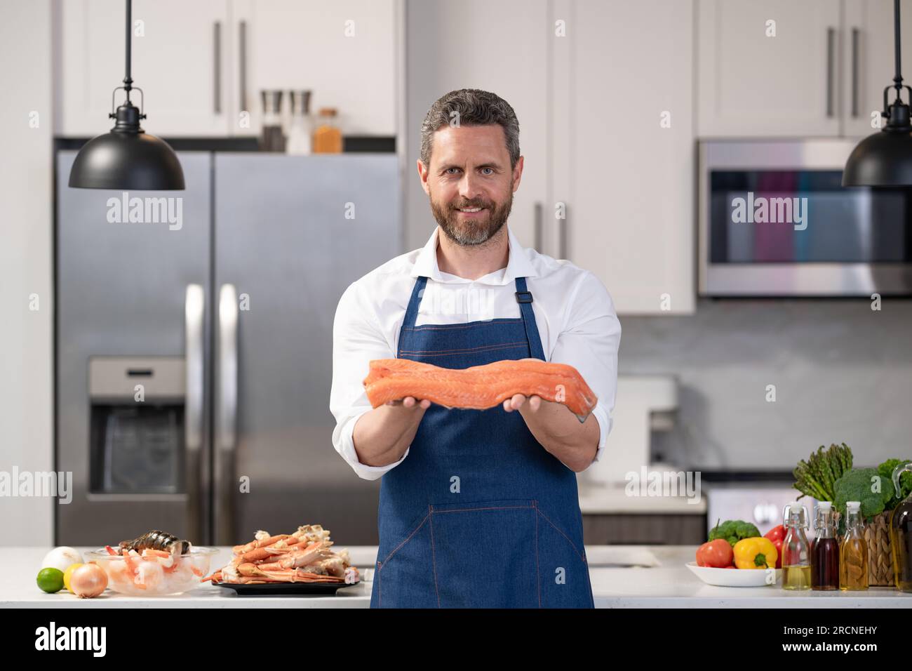happy chef man cooking fish. chef man cooking fish salmon. chef man cooking fish in the kitchen. photo of chef man cooking fish. Stock Photo