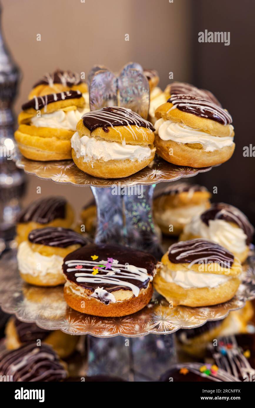 profiterole and eclairs with wiped cream and glazed with chocolate and fondant , kids birthday party, on a shiny display tower sited on a table Stock Photo