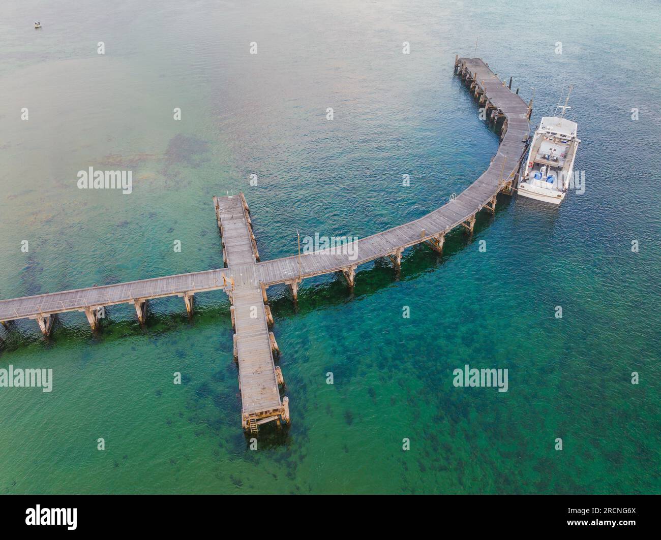 A lone fishing boat tied to a curved jetty over a calm bay at Venus Bay