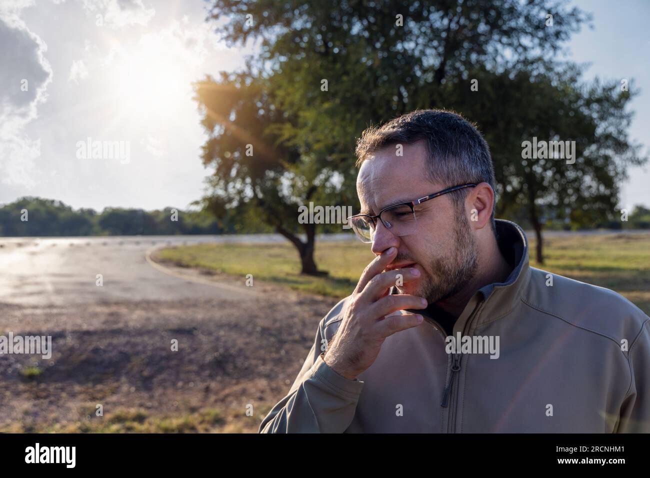 caucasian man with glasses and a beard, standing outside the car on the road, worried about what just happened Stock Photo