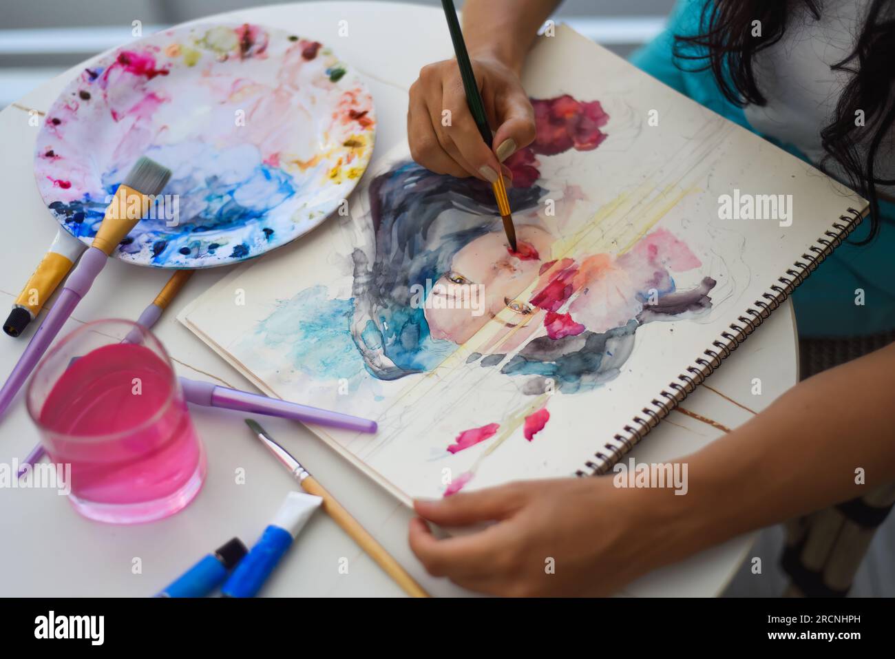 Woman painting watercolor drawing of asian girl with brush on a table with water and paints Stock Photo