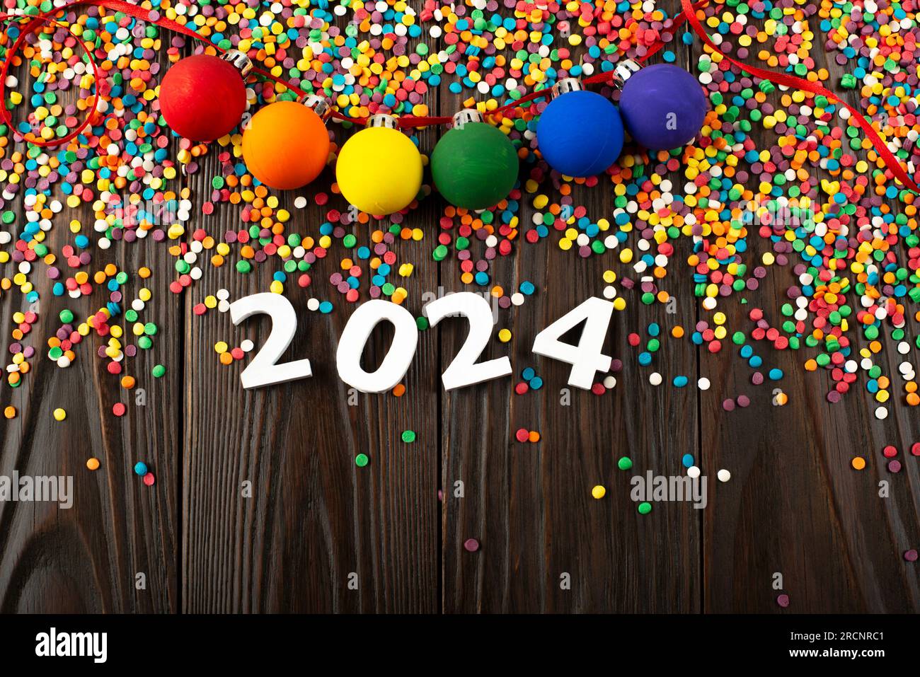 White numbers 2024 and color sugar sprinkles on wooden table with color balls garland Stock Photo