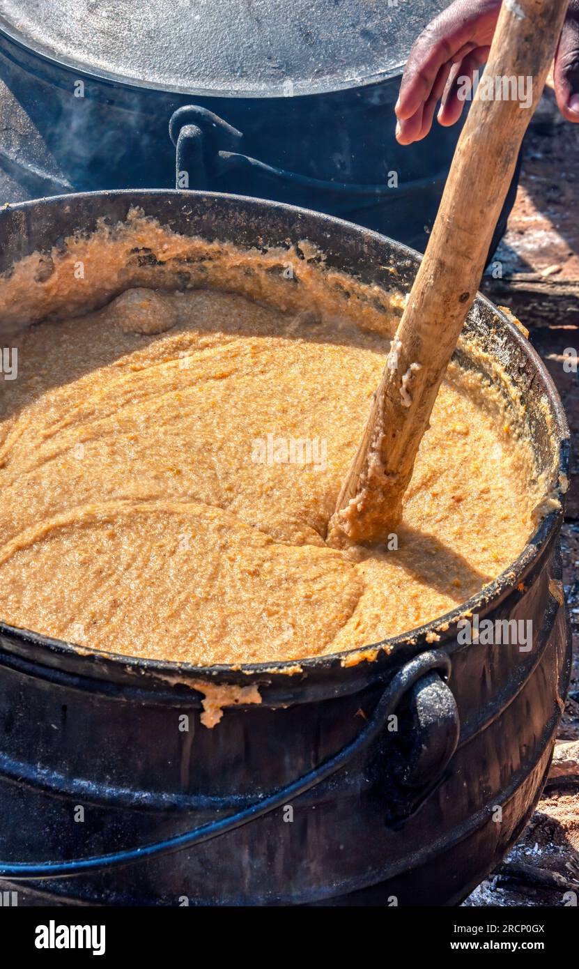 African cooking outdoors ,huge pot of porridge pap in a cast iron pot, man with a wooden spoon mixing Stock Photo