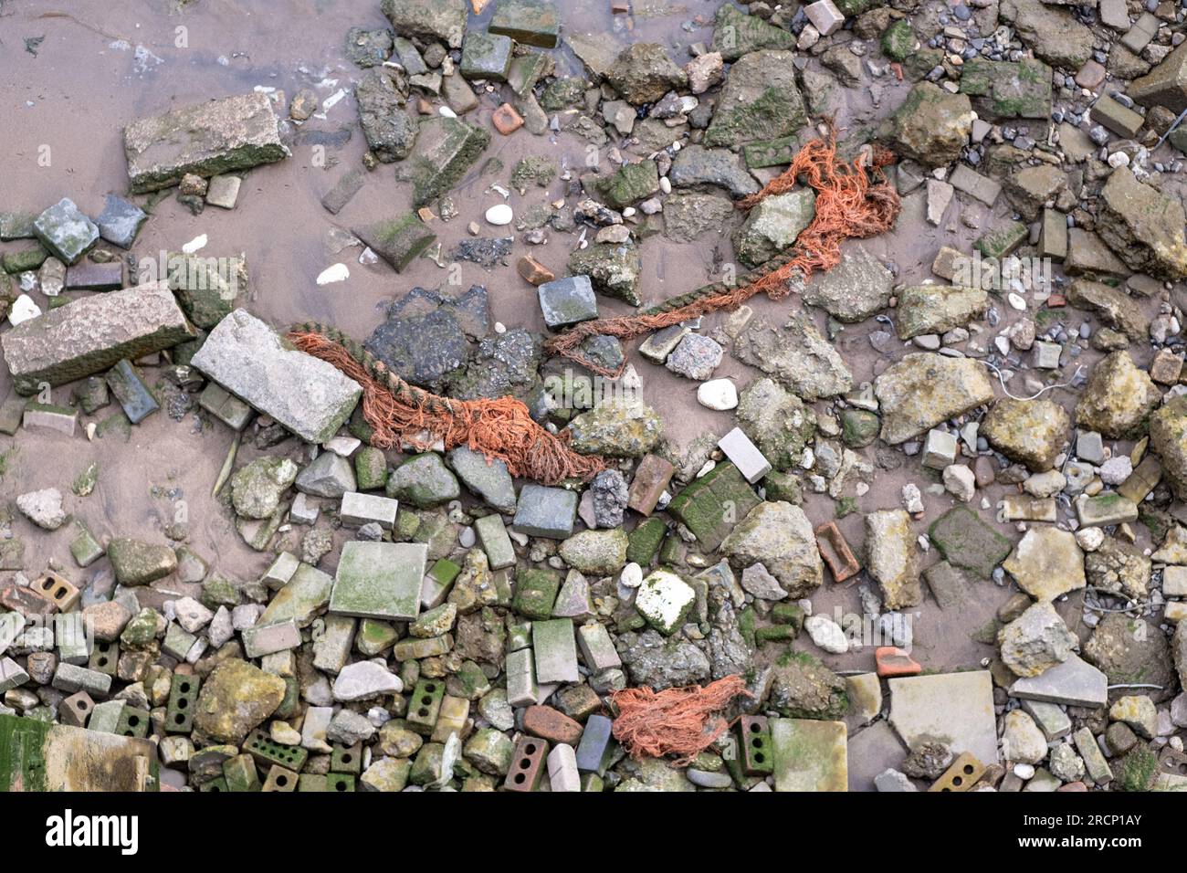 Old rope, bricks and rocks strewn on the River Thames foreshore, river ...