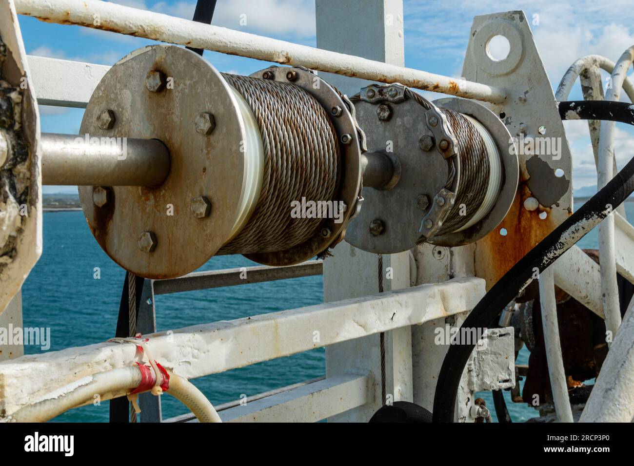 Close-up of winch with coiled cable on a ship deck against a blue sea and sky, Irish Sea, UK Stock Photo