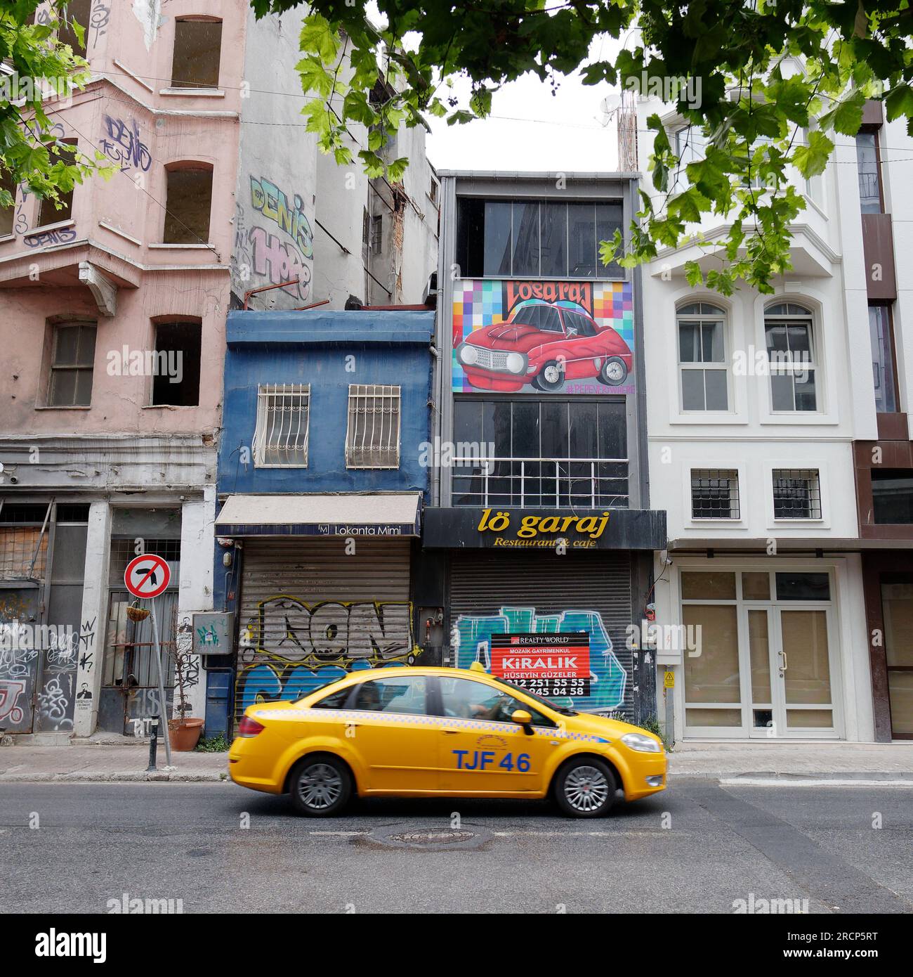 Yellow taxi on a street with shuttered down shops in the Karakoy neighbourhood of Istanbul with a ed car illustrated on the wall of a building. Turkey Stock Photo