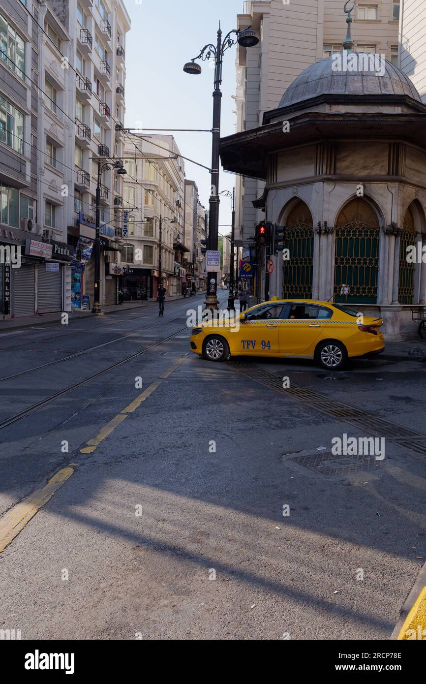 Yellow Taxi at a road junction in Istanbul on a summers morning as someone rides a scooter in the middle of the road. Turkey Stock Photo