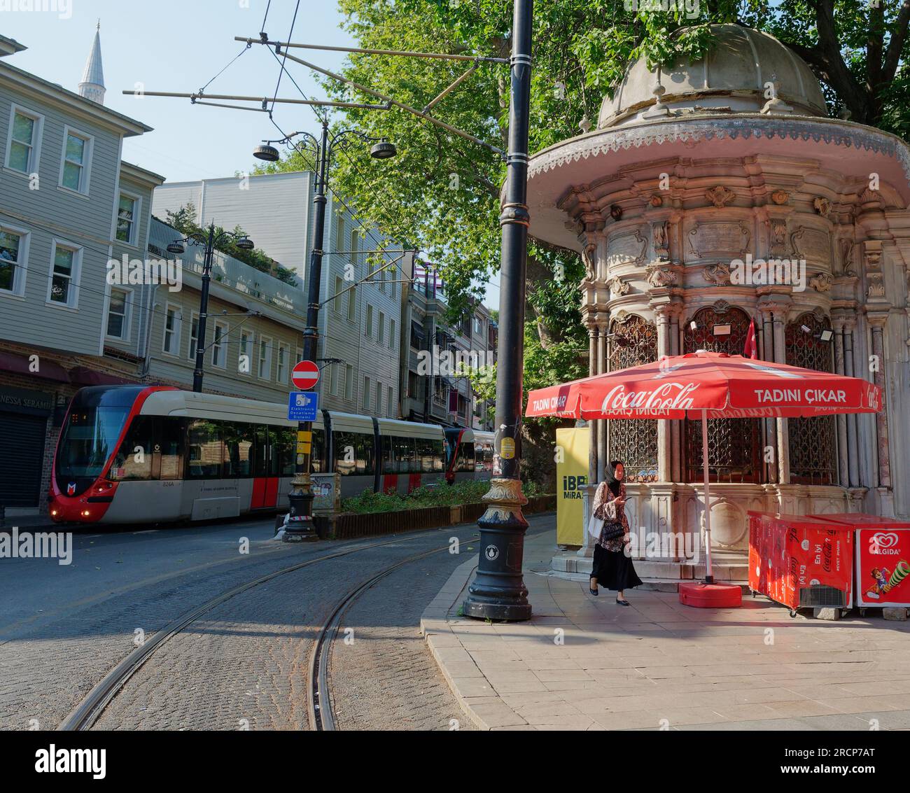 Muslim lady walks beside a Art Nouveau Kiosk with a metro tram opposite in Istanbul, Turkey on a summers morning Stock Photo
