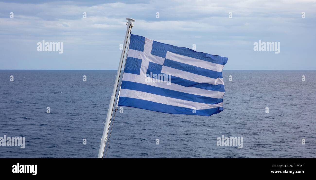 Greece sign symbol of leading shipping power in the world. Greek flag on flagpole waving over rippled sea water. Cloudy sky background. Stock Photo