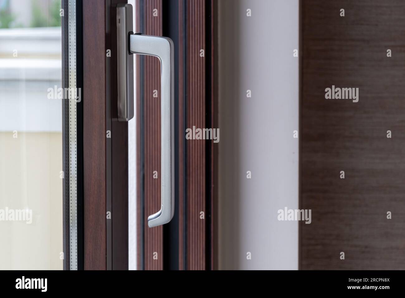Aluminum silver handle on close window, door against brown frame