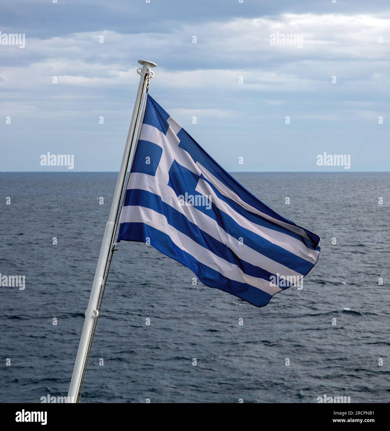 Greece sign symbol of leading shipping power in the world. Greek flag on flagpole waving over rippled sea water. Cloudy sky background. Stock Photo