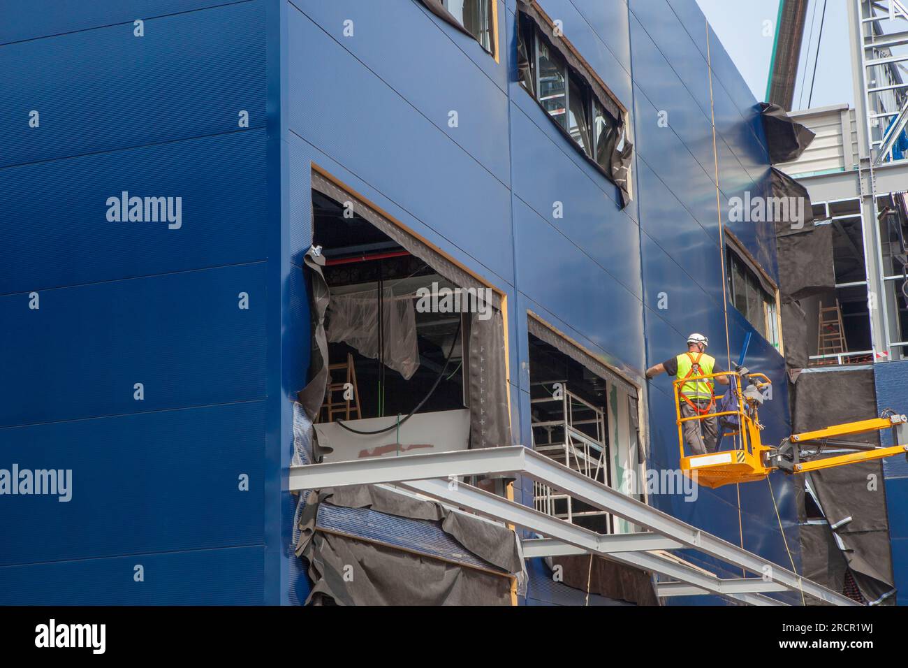 Worker installing insulating panels in a building under construction. He is over telehander crane Stock Photo