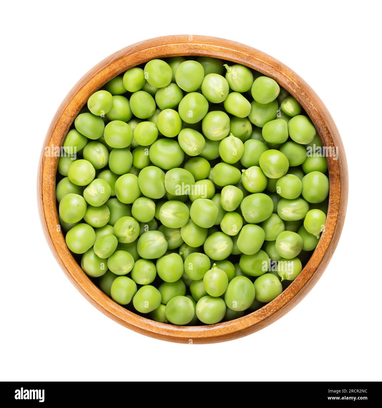 Fresh green peas, in a wooden bowl. Raw, small spherical seeds of the pod fruit Pisum sativum of greenish and yellowish color, mostly used for soups. Stock Photo