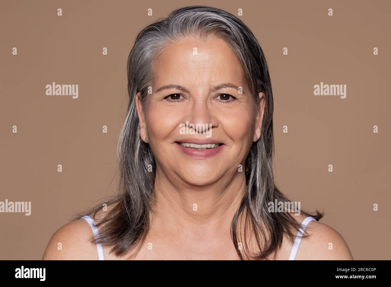 Glad elderly caucasian lady with gray hair, enjoys anti-aging treatment, isolated on brown background Stock Photo