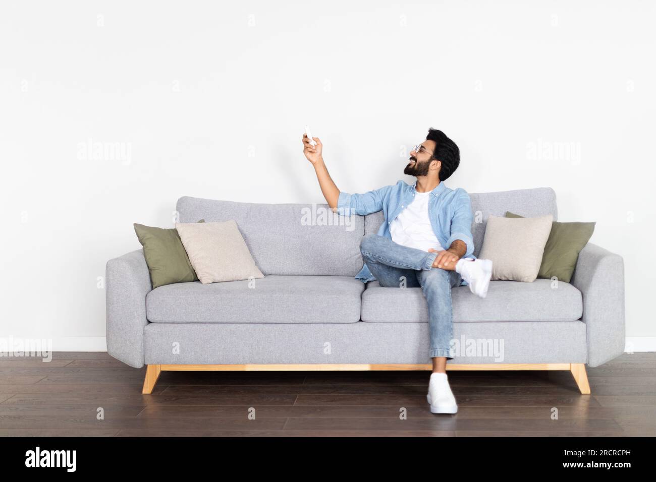 relaxed-middle-eastern-guy-chilling-on-couch-turning-on-ac-stock-photo