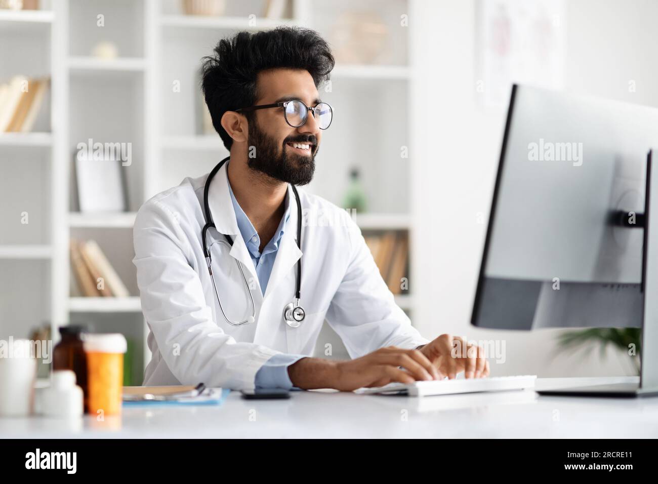Arab man general practitioner look at computer screen, consult patient Stock Photo