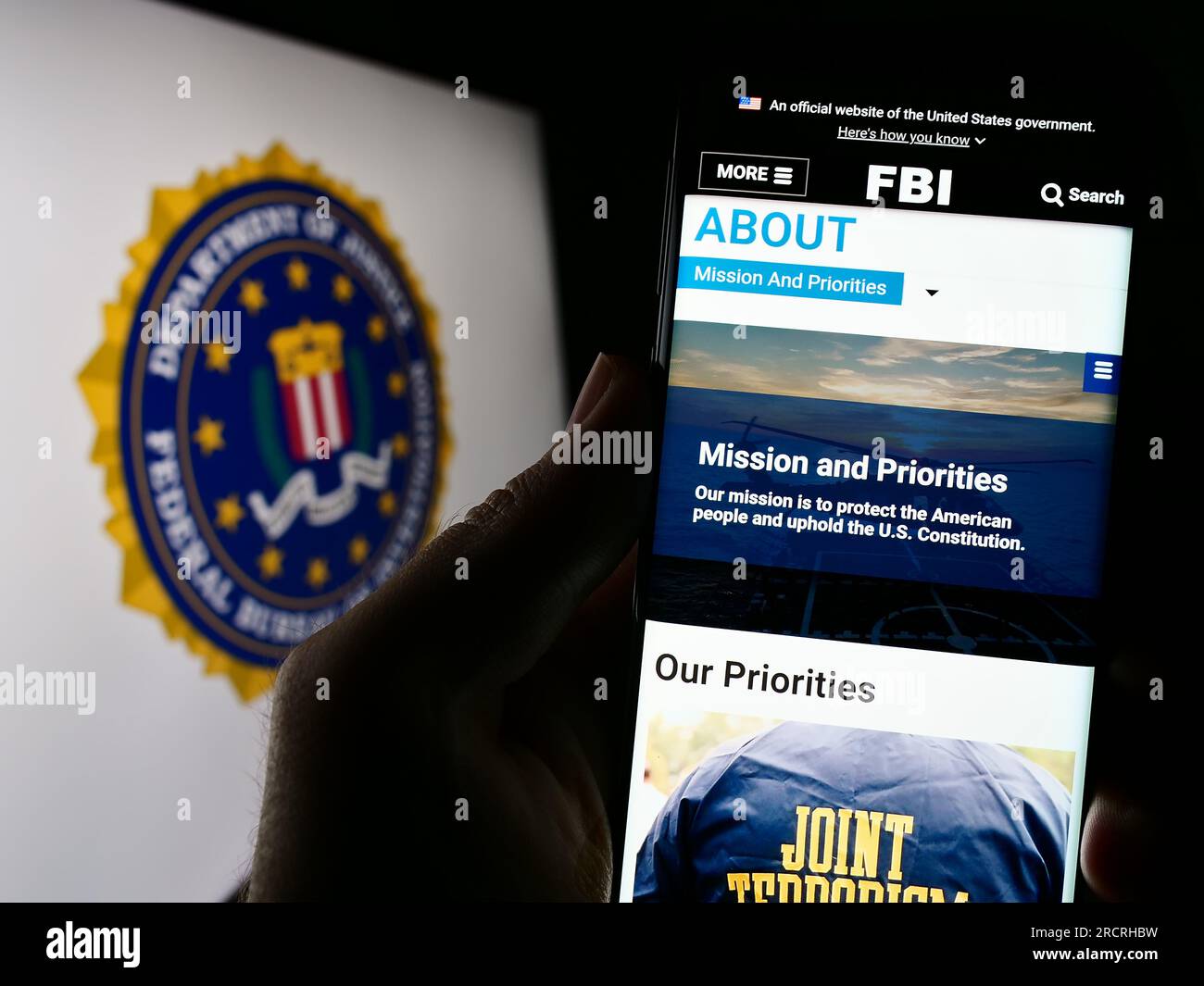 Person holding cellphone with webpage of US Federal Bureau of Investigation (FBI) on screen in front of seal. Focus on center of phone display. Stock Photo