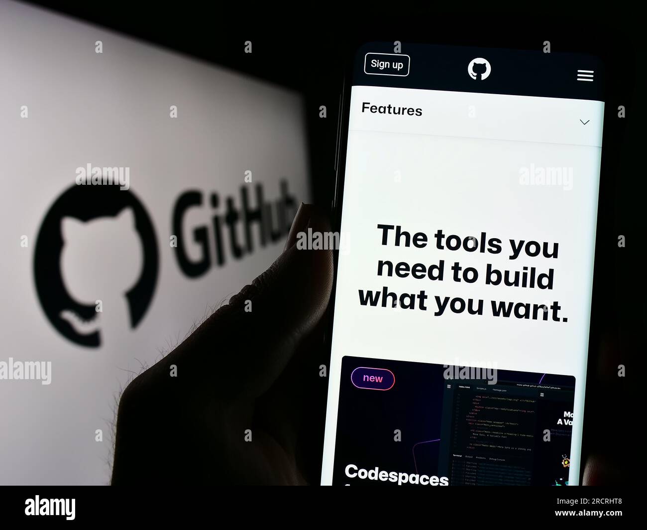 Person holding smartphone with website of US software development company GitHub Inc. on screen with logo. Focus on center of phone display. Stock Photo