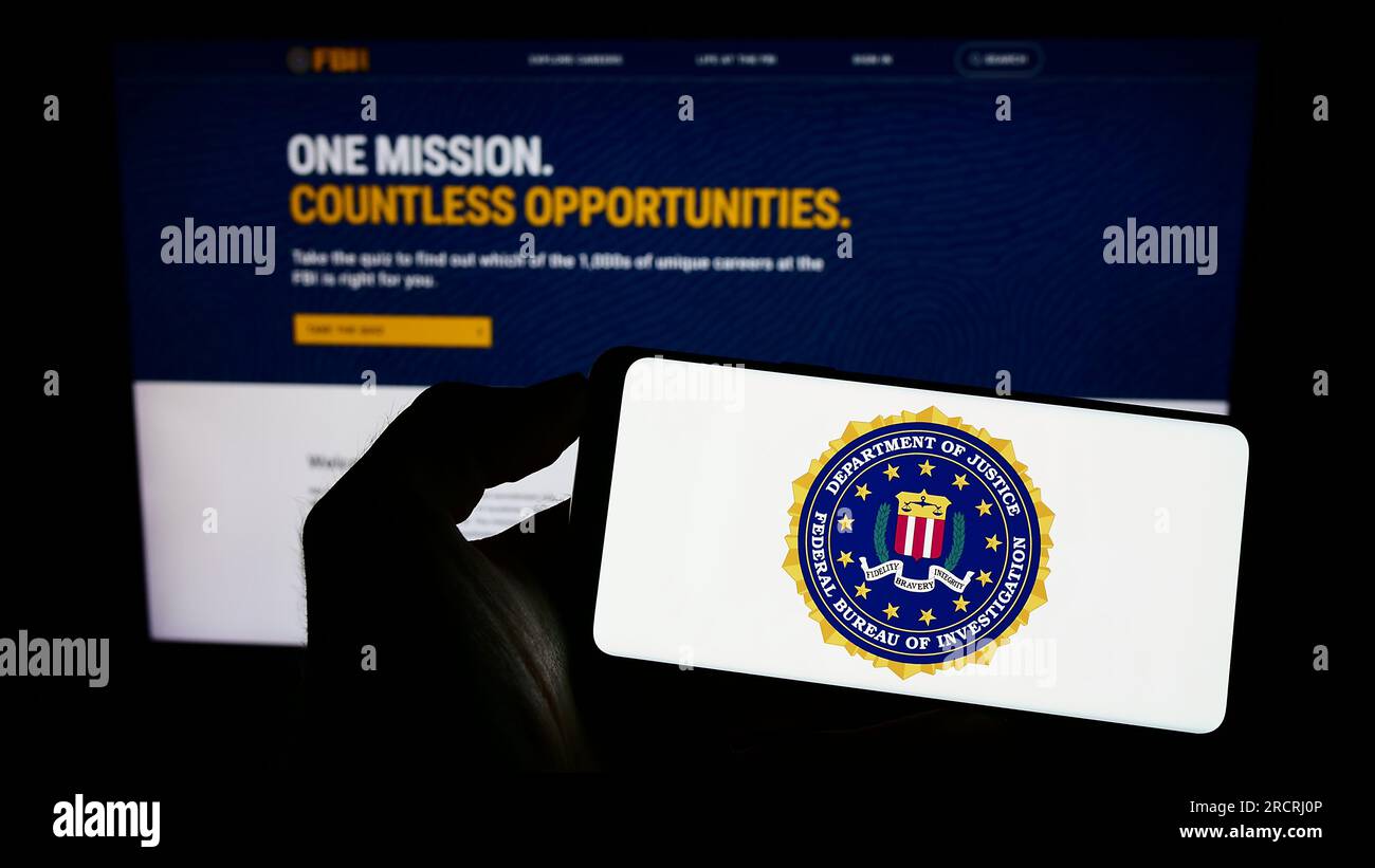 Person holding smartphone with seal of US Federal Bureau of Investigation (FBI) on screen in front of website. Focus on phone display. Stock Photo