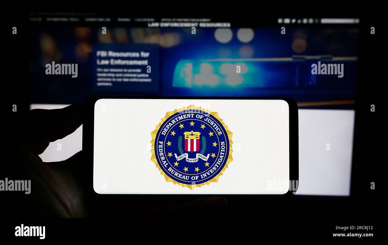 Person holding cellphone with seal of American Federal Bureau of Investigation (FBI) on screen in front of webpage. Focus on phone display. Stock Photo
