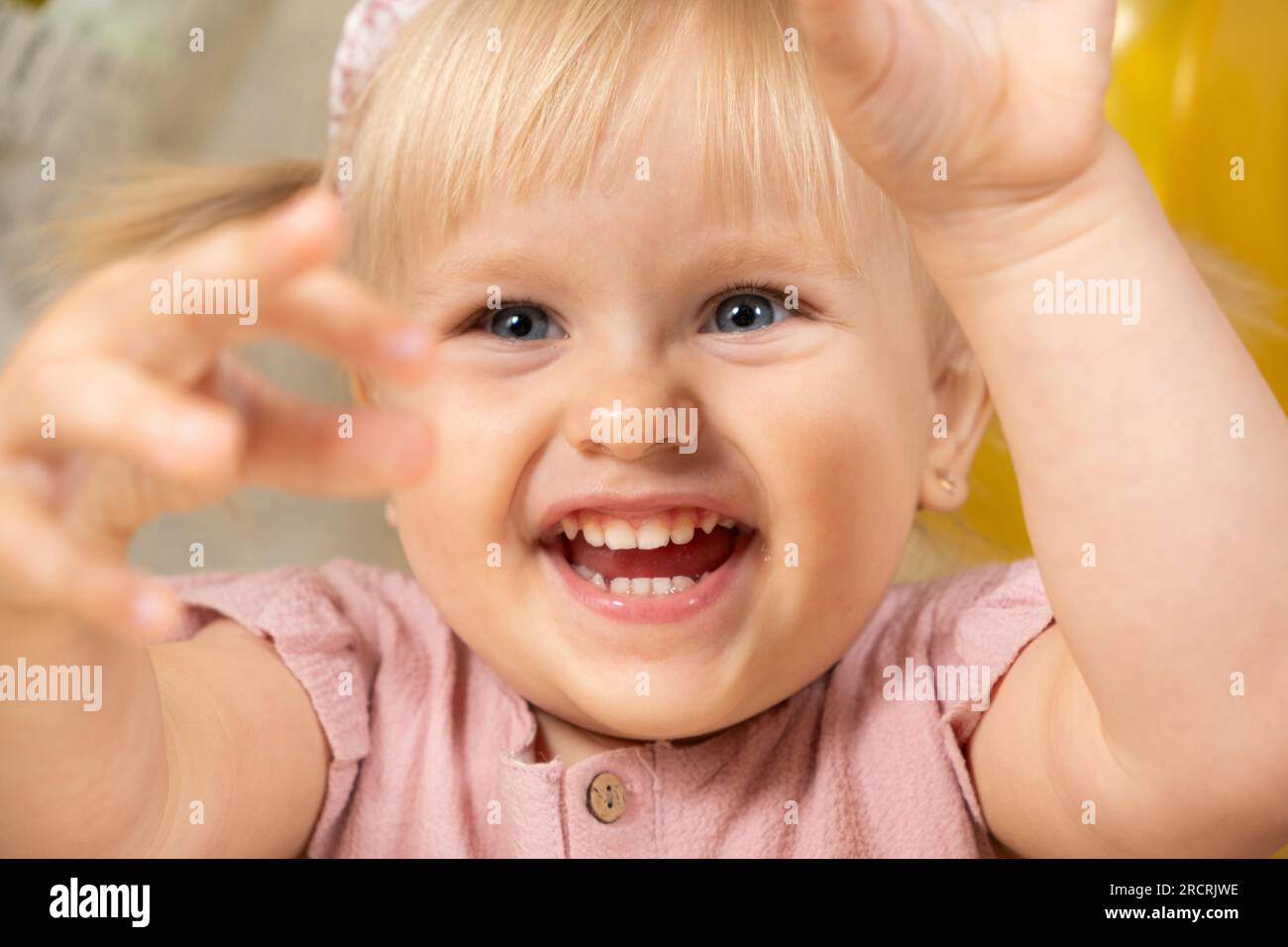 Portrait of a laughing twoyearold girl waving her arms upwards Stock