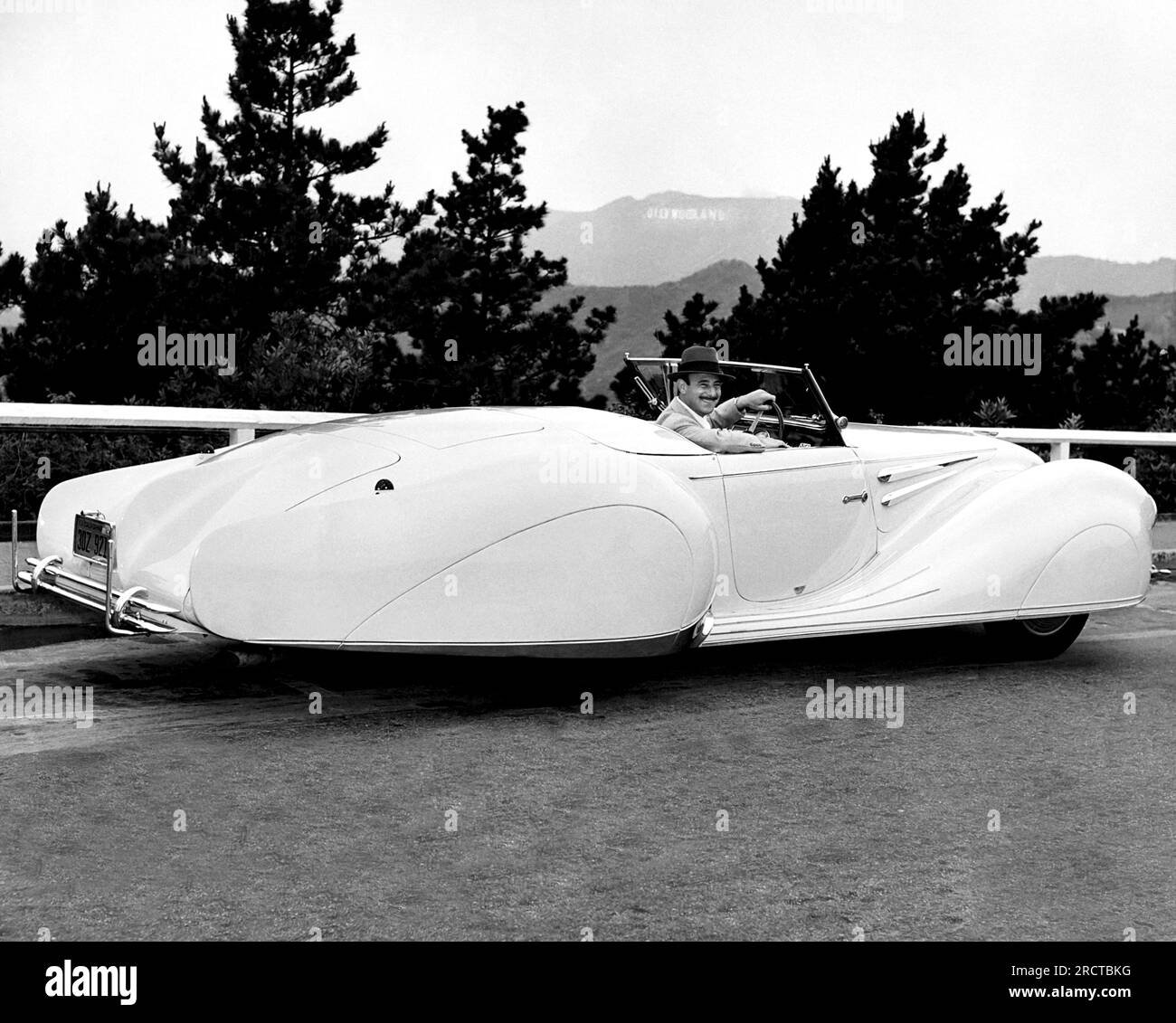 Los Angeles, California:  1949 A man in a 1949 Delahaye coupe with the Hollywood sign visible in the hills behind. Stock Photo