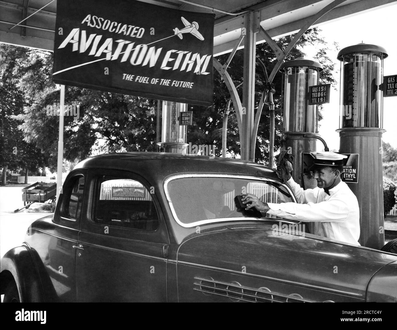 United States:  c.  1938 A gas station attendent cleans a customer's automobile windshield as the car is filled with 19Â¢ a gallon gas. Stock Photo