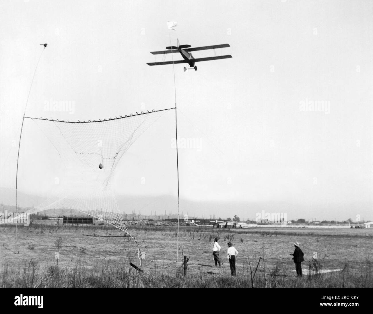 Whittier, California:  c. 1926 A new invention for delivering air mail to airports has been proven to work. The mail sack is lowered down on a rope by the pilot and carried into a 40' x 40' net that is equipped with a series of sharp knives on the upper rim, which cut the rope and the mail bag then rolls gently to the ground. Stock Photo