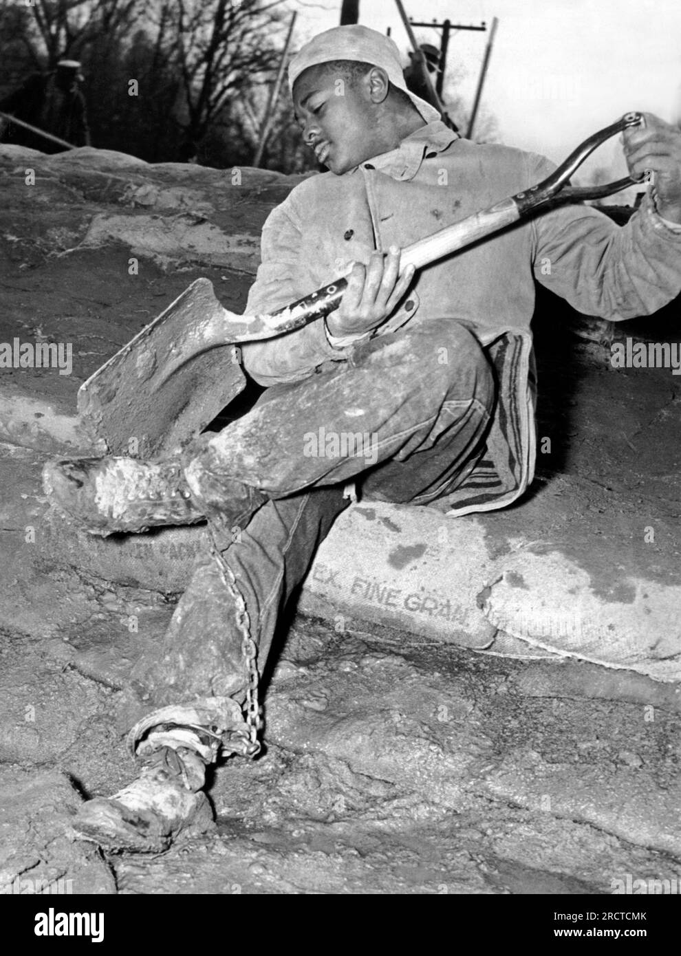Memphis, Tennessee:   February 2, 1937 A chain gang prisoner from the Shelby County Penal Farm pauses to clean his shoes while sandbagging a Mississippi River levee. Stock Photo