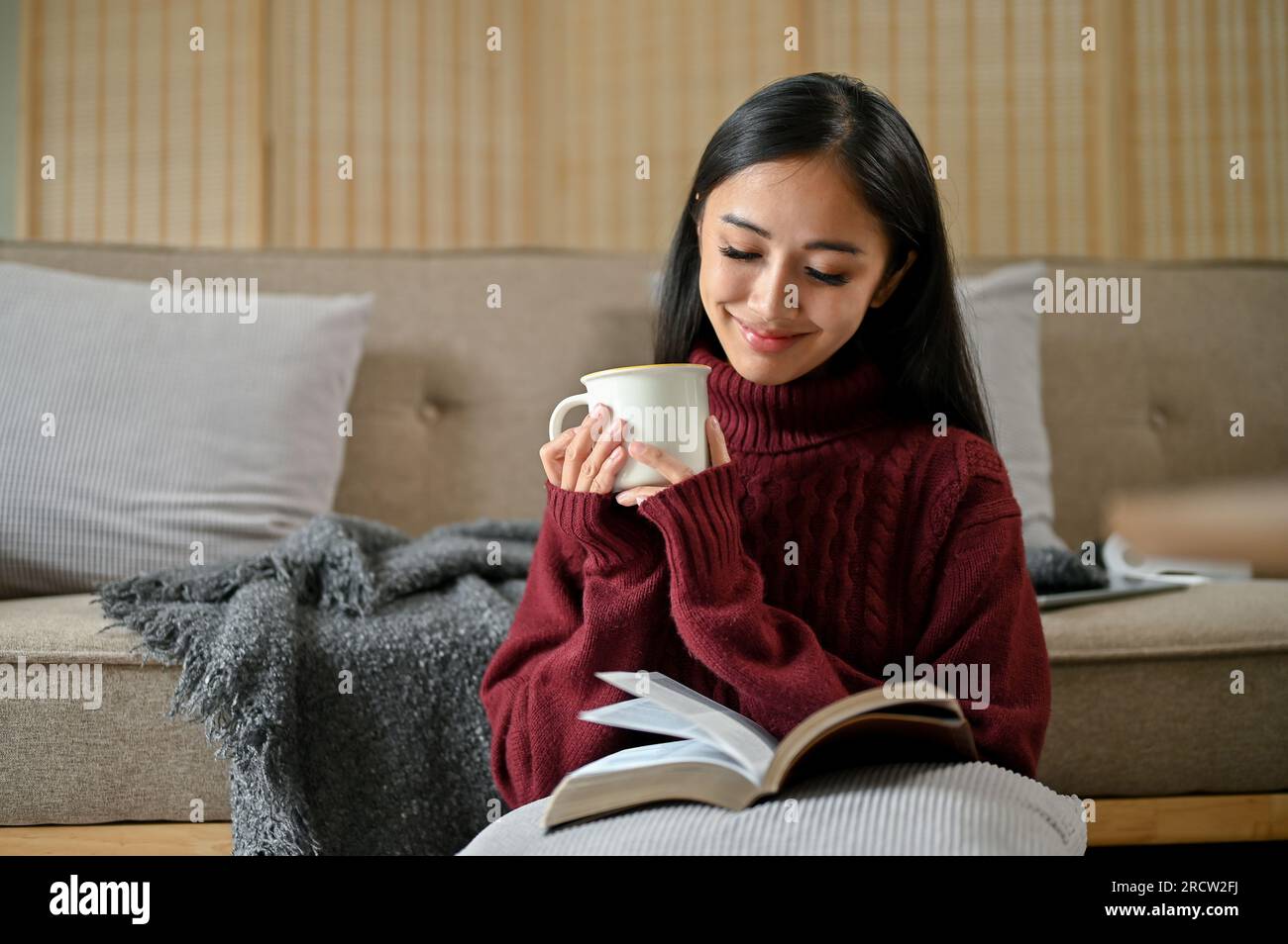 A pretty and relaxed Asian woman in a cozy sweater enjoys her morning ...