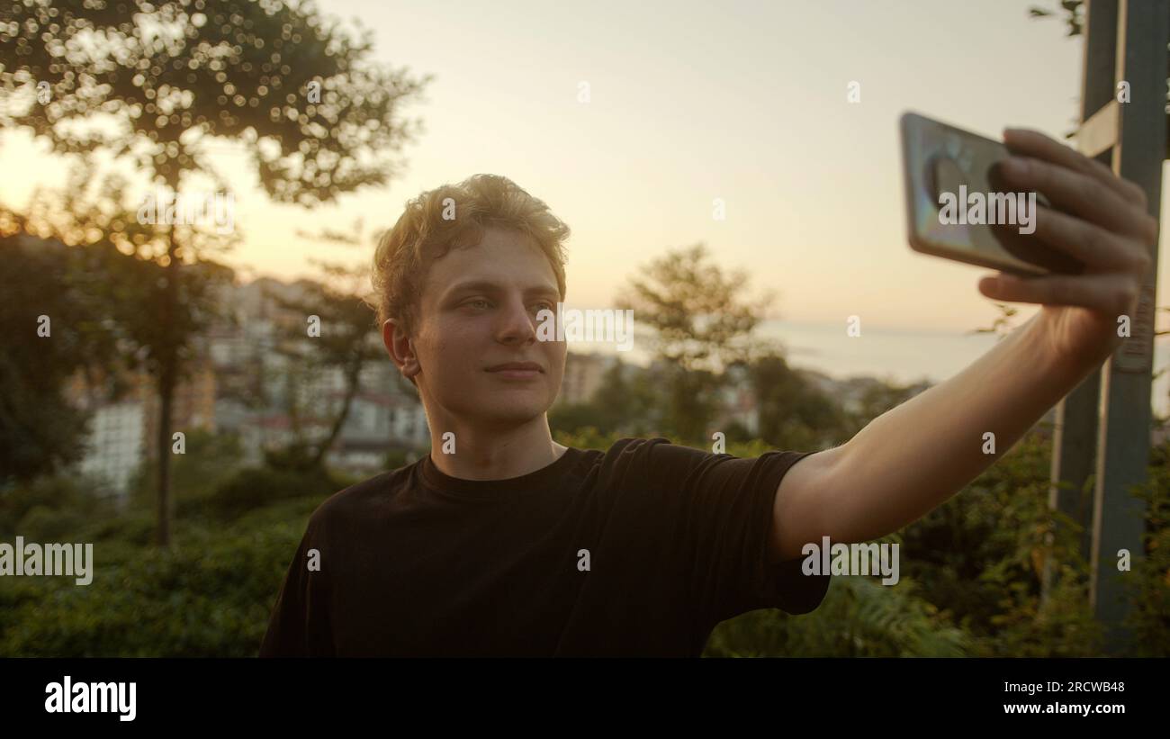 Blond Young Man Taking Selfies with His Smartphone, Striking Various Poses Outdoors Stock Photo